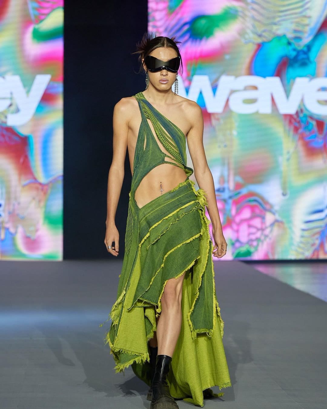 Model in a green cut-out look walking the WAVEY runway in front of iridescent LED walls